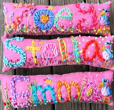 two pink embroidered pillows sitting on top of a wooden table