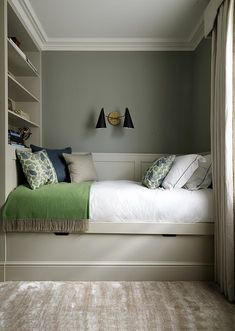 a bed sitting under a window next to a book shelf filled with books and pillows