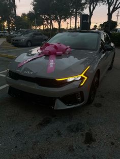 a gray car with a pink bow on it's hood parked in a parking lot