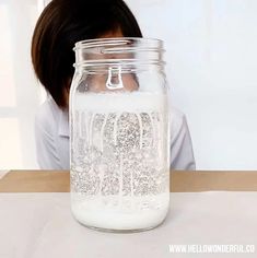 a woman sitting at a table with a jar on her head in front of her