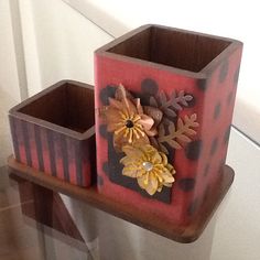 a red vase with flowers and leaves sitting on top of a wooden shelf next to a mirror