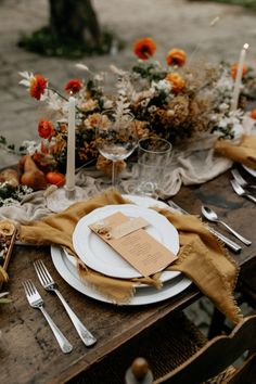 the table is set with white plates, silverware and orange floral centerpieces