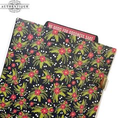 a black notebook with red and green flowers on the cover, sitting next to a white background