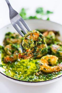 a fork full of broccoli and shrimp being lifted from a bowl with pesto sauce