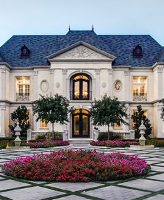 a large white house with lots of windows and flowers in the front garden area at dusk