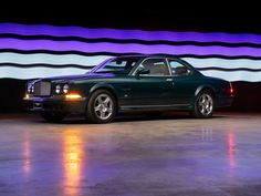 a green car parked in front of a purple and white wall with lights on it