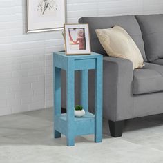 a blue end table with a white vase on it in front of a gray couch