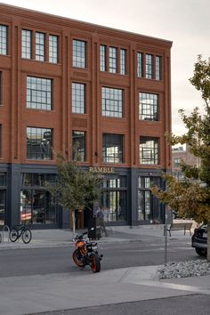 an orange motorcycle parked in front of a tall brick building with lots of windows on it