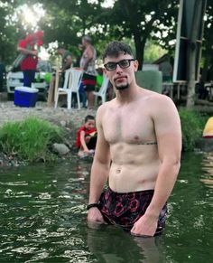 a shirtless man standing in the middle of a body of water with his hands on his hips