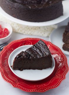 a slice of chocolate cake on a red and white plate next to two plates with raspberries