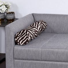 a gray couch with a zebra print pillow on it next to a table and vases