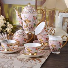 pink and gold tea set with matching saucers, cups and spoons on a table