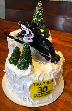 a cake with a snowmobile and trees on it that says caution 30 is in the background