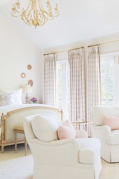 a bedroom with white furniture and chandelier hanging from the ceiling in front of two windows