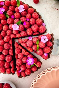 a chocolate cake with raspberries and flowers on the top is cut into slices