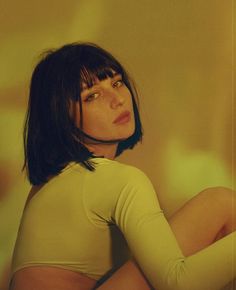 a woman with short hair wearing a yellow shirt and green tights sitting on the floor