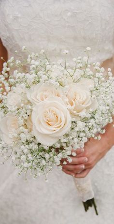 a bride holding a bouquet of white roses and baby's breath in her hands