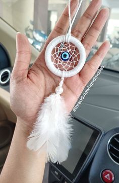 a hand holding a white dream catcher with an evil eye on it