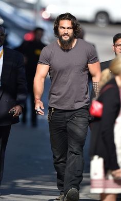 a man with long hair and beard walking down the street in front of other people