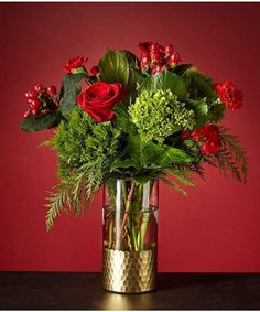 a vase filled with red roses and greenery on top of a wooden table next to a red wall