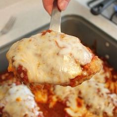 a person holding a spoon full of cheese covered meatballs