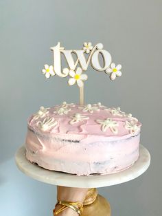 a person holding a cake with the word two spelled out in white letters on top