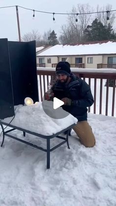 a man kneeling down in the snow next to an outdoor grill with lights on it