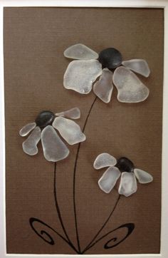 three glass flowers on a brown background in a white frame with black stones and silver accents