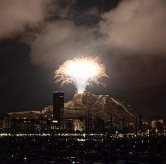 fireworks are lit up in the sky above a city at night with mountains in the background