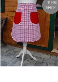 a white mannequin wearing a red and white checkered apron with pockets on it