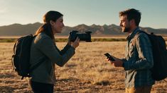 a man standing next to a woman holding a camera in front of her on a field