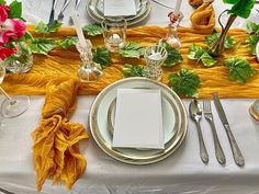 the table is set with silverware, napkins, and flower arrangements on it