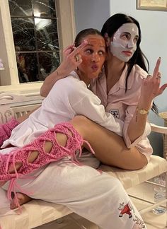 two women sitting on a bed with their faces painted like they are making the peace sign