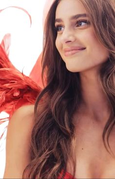 a woman with long brown hair and red wings on her chest smiling at the camera