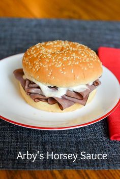 a hamburger with meat and cheese is on a plate next to a red napkin that says arby's horsey sauce