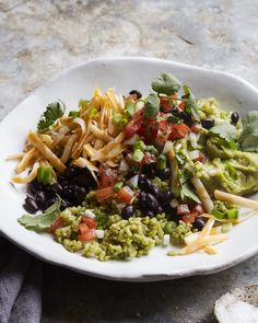 a white plate topped with black beans, guacamole and tortilla chips