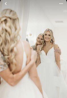 two women in white dresses are looking at their reflection in the mirror while another woman is taking her picture