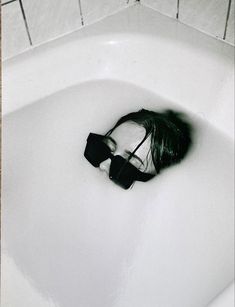 a black and white photo of a person in a bathtub with sunglasses on their head