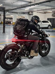 a man riding on the back of a red motorcycle in a parking garage next to parked cars