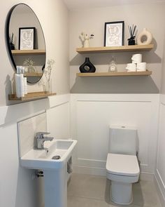 a white toilet sitting next to a sink in a bathroom under a mirror and shelves