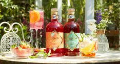 three bottles of alcohol sitting on top of a table next to bowls and glasses filled with fruit