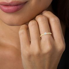 a woman wearing a gold ring with a diamond on the middle and a thin band around her finger