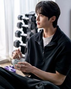 a young man sitting on the floor holding a bowl and looking at something in front of him