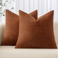 two brown pillows sitting on top of a white couch next to a potted plant