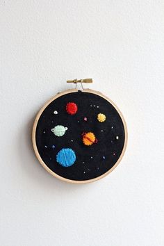 an embroidery project with planets and stars on the black fabric, hanging on a white wall