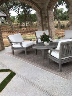 an outdoor patio with chairs and tables on the ground near brick pillars, surrounded by trees