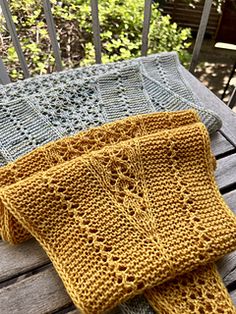 two knitted scarves sitting on top of a wooden bench