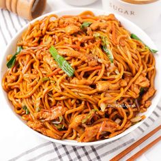 a white bowl filled with chinese noodles and sauce next to chopsticks on a table