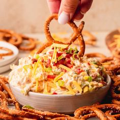 a person dipping some food into a bowl with pretzels on the table next to it