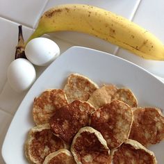 some pancakes on a plate next to an egg and a banana in the background,